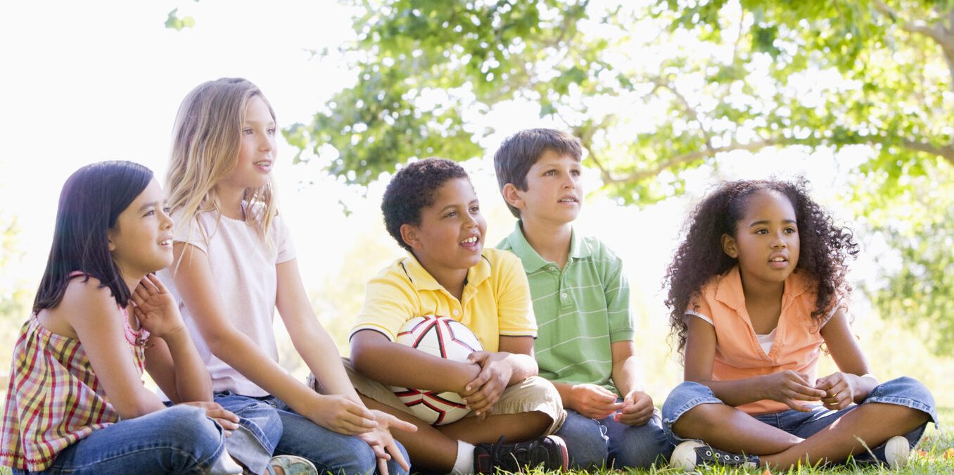 Five young friends sitting outdoors with soccer ball