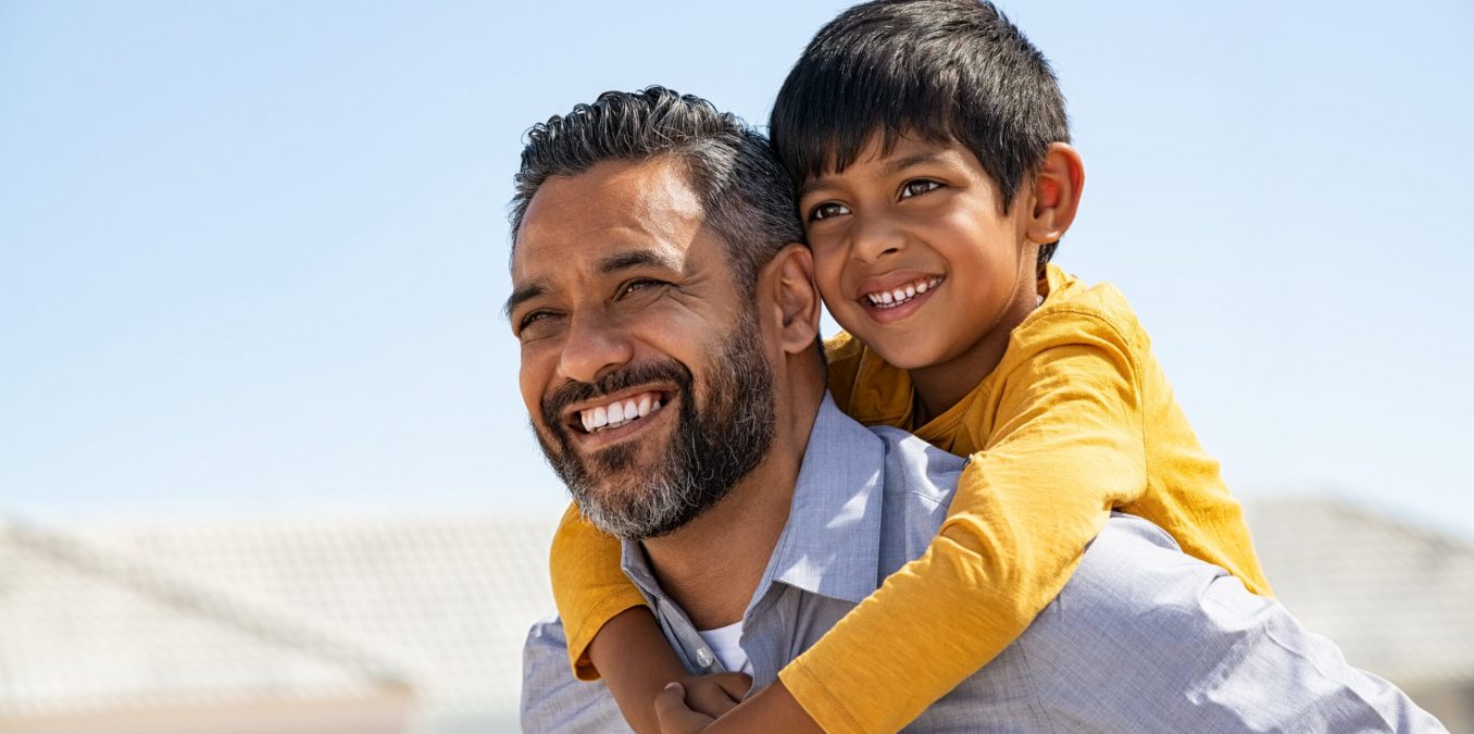 A smiling father and son sharing a piggyback ride outdoors.
