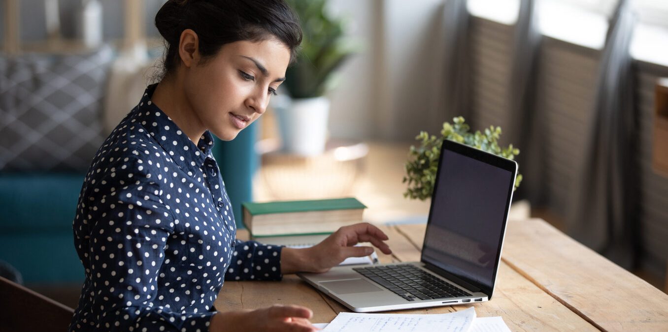 Millennial Indian girl sit at desk in living room study