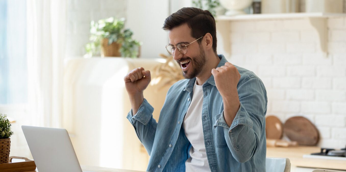 Happy guy celebrate great news opportunity got read by e-mail. Excited man sit in kitchen look at laptop screen with clenched fists feels incredible amazed received good notice. Sale, discount concept