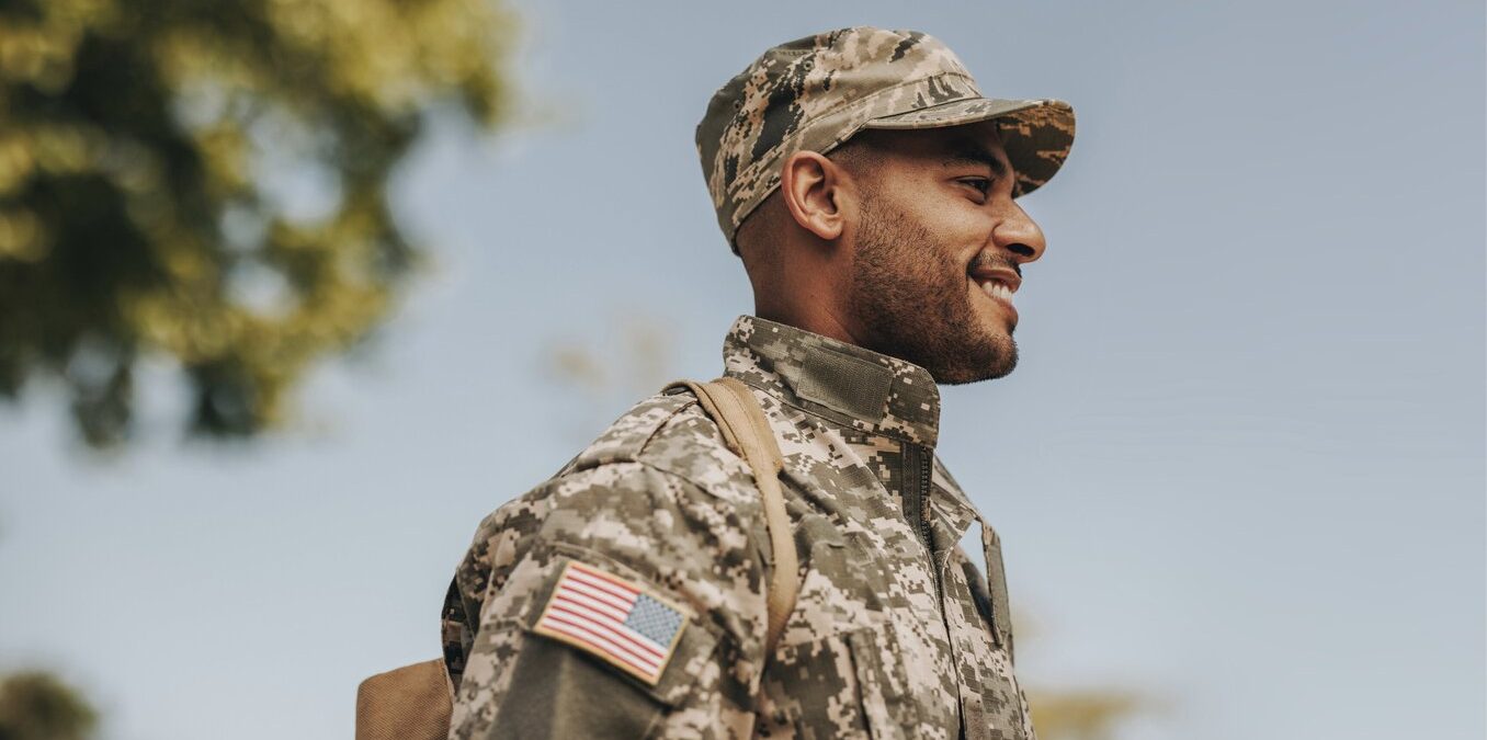 Happy young soldier smiling cheerfully while standing outside his home. Patriotic American serviceman coming back home after serving his country in the military.
