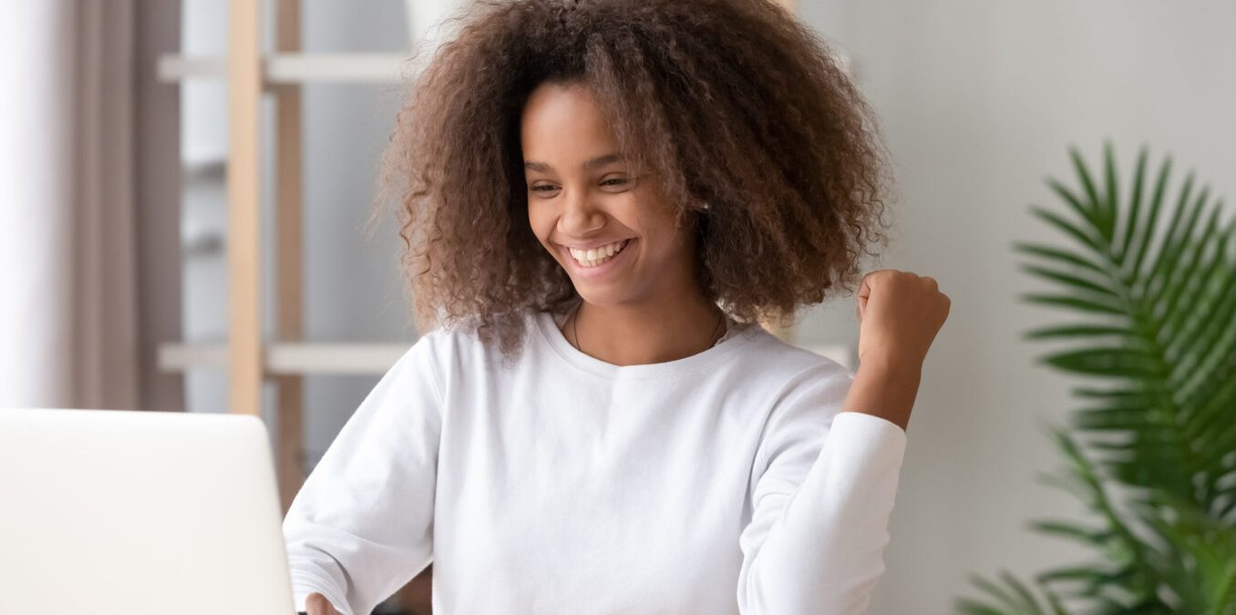 A happy young student celebrating while looking at her laptop