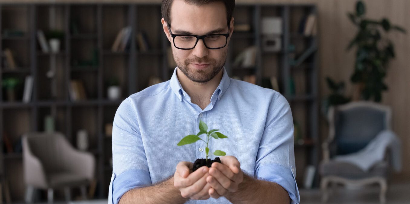 Happy young businessman holding soil green plant