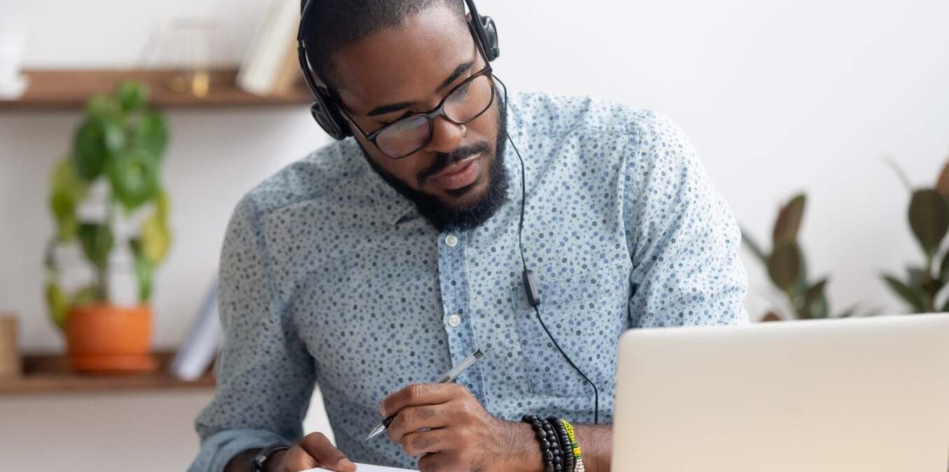 A man focused on his laptop while taking notes