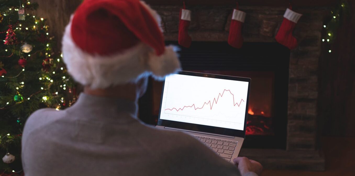 Man wearing a Santa Claus hat looking at a chart on a laptop