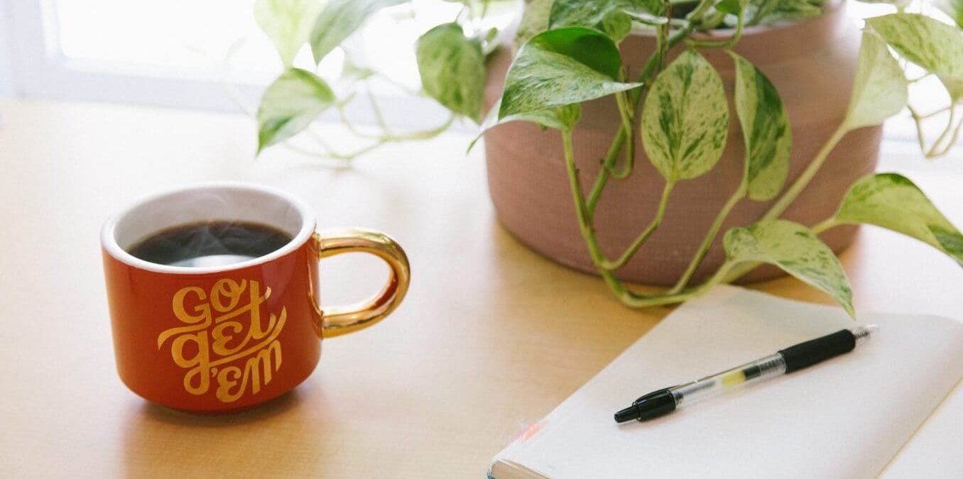 Mug reading "Go Get 'Em" sits next to an open journal with a pen.