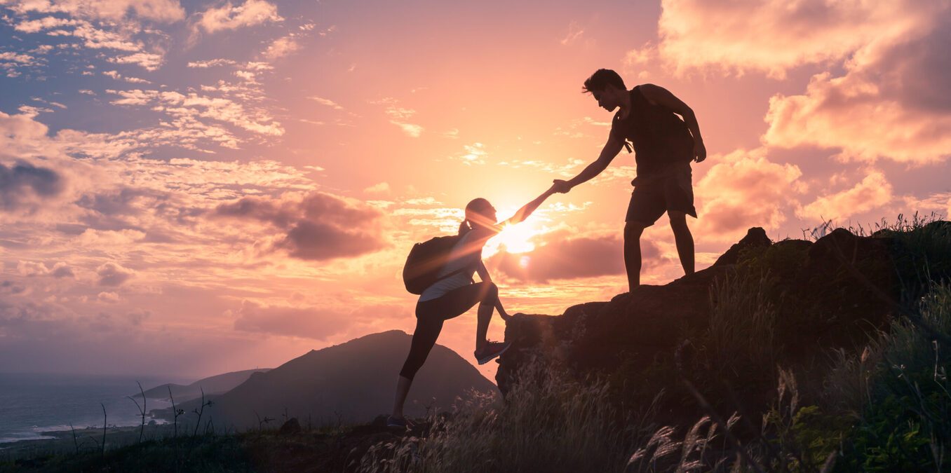 People helping each other hike up a mountain at sunrise. Giving a helping hand, and active fit lifestyle concept.