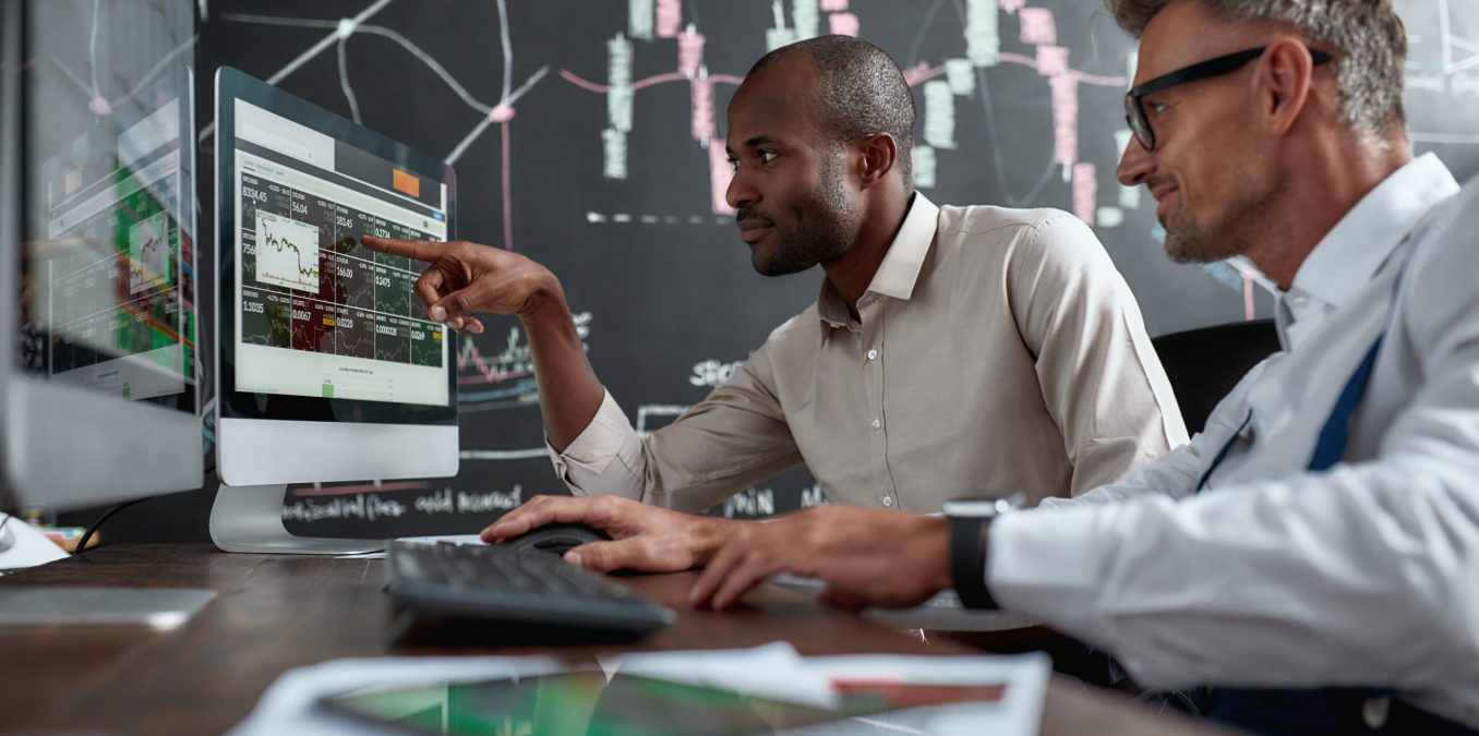 Two,Diverse,Colleagues,Traders,Talking,To,Each,Other,,Looking,At