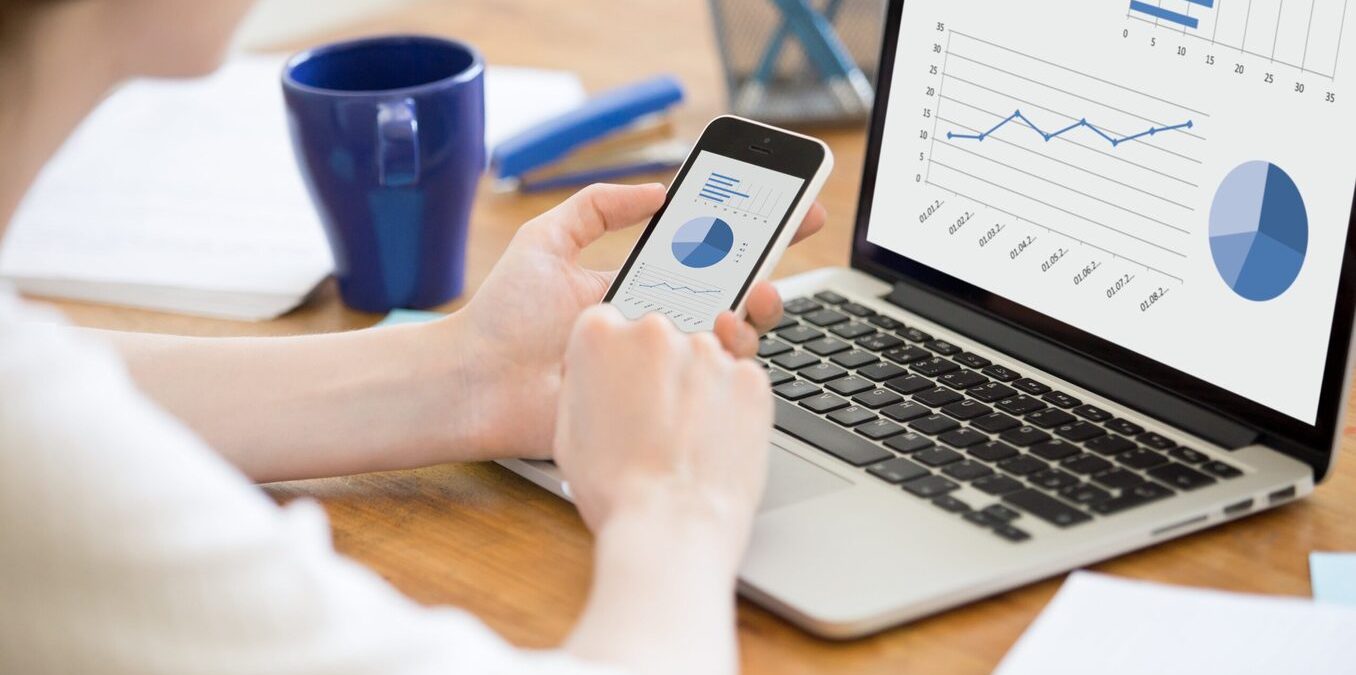 Person reviewing charts on their phone and laptop