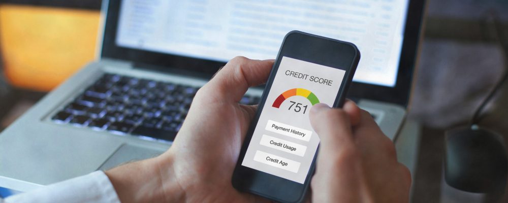 picture of a man's hands holding a smartphone with credit score displayed on the screen with a laptop in the background