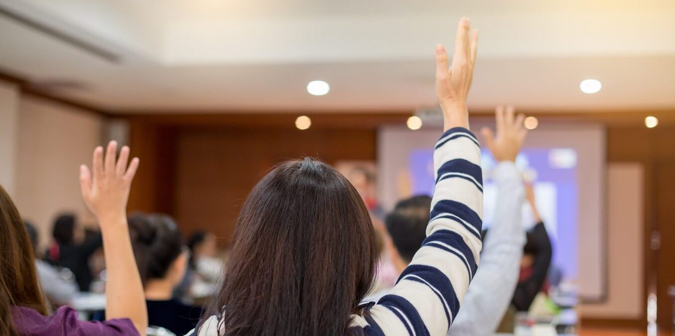 Room full of people raising hands during a lecture or presentation