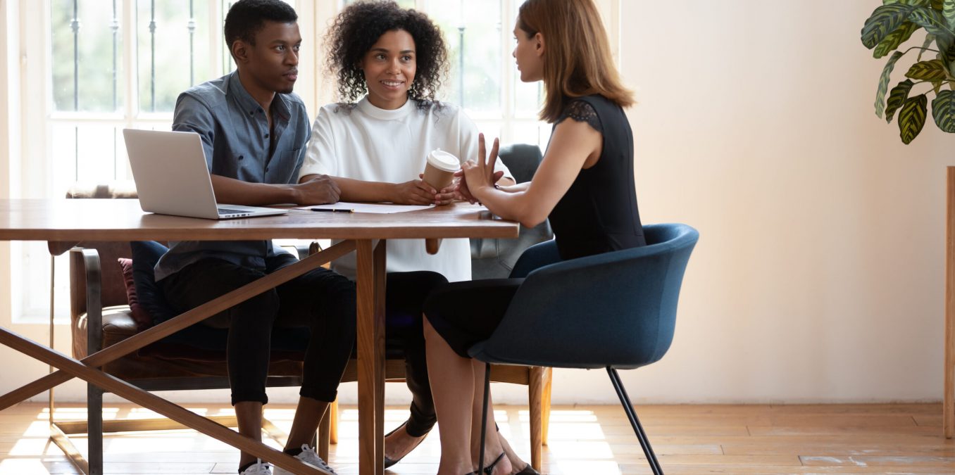 Young,African,American,Husband,And,Wife,Sit,At,Desk,Talk