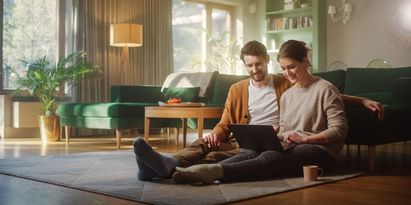 Couple,Use,Laptop,Computer,,While,Sitting,On,The,Living,Floor