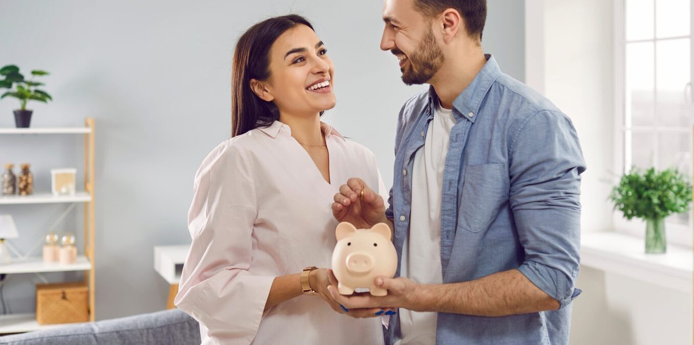 Smiling happy young family together put coins in piggy bank