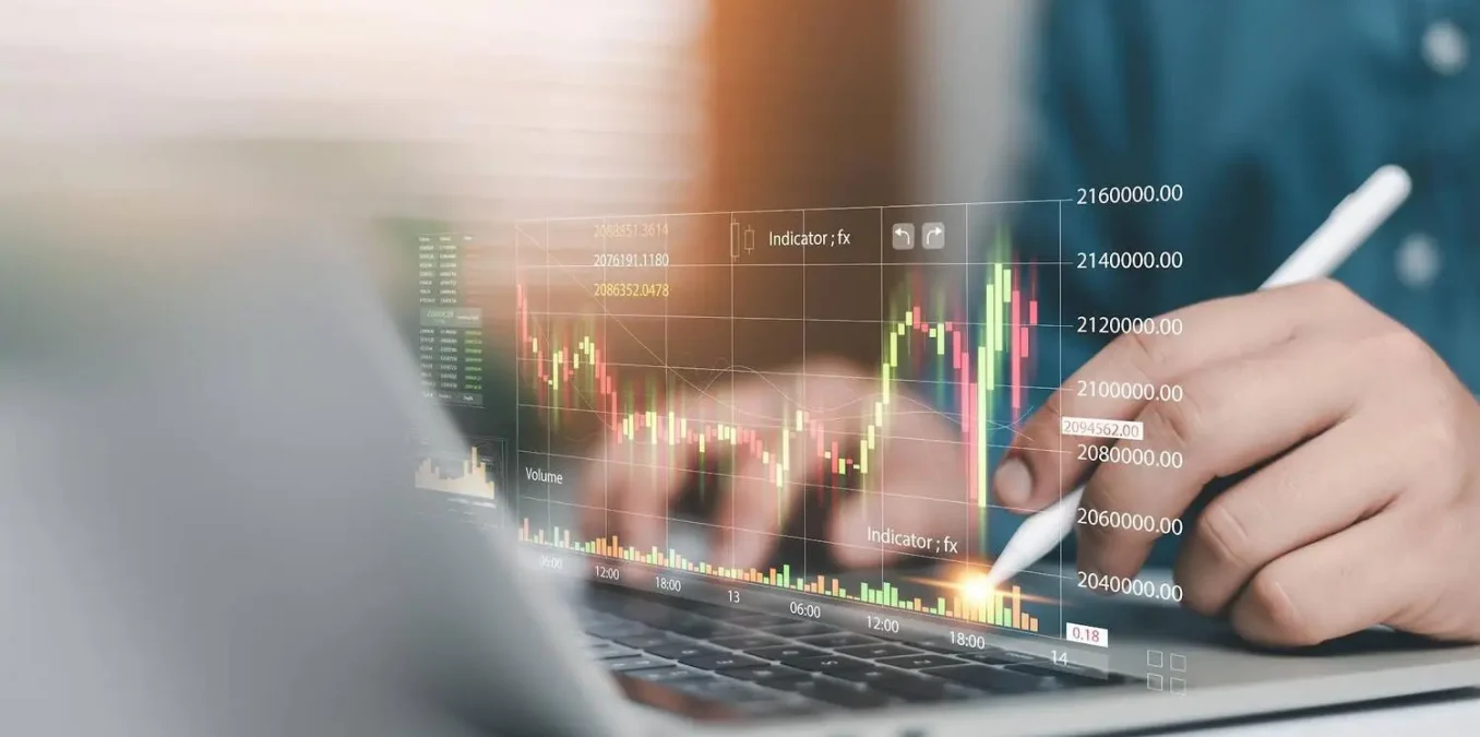A trader using a stylus on a laptop to analyze interactive stock market charts, candlestick graphs, and financial data indicators.