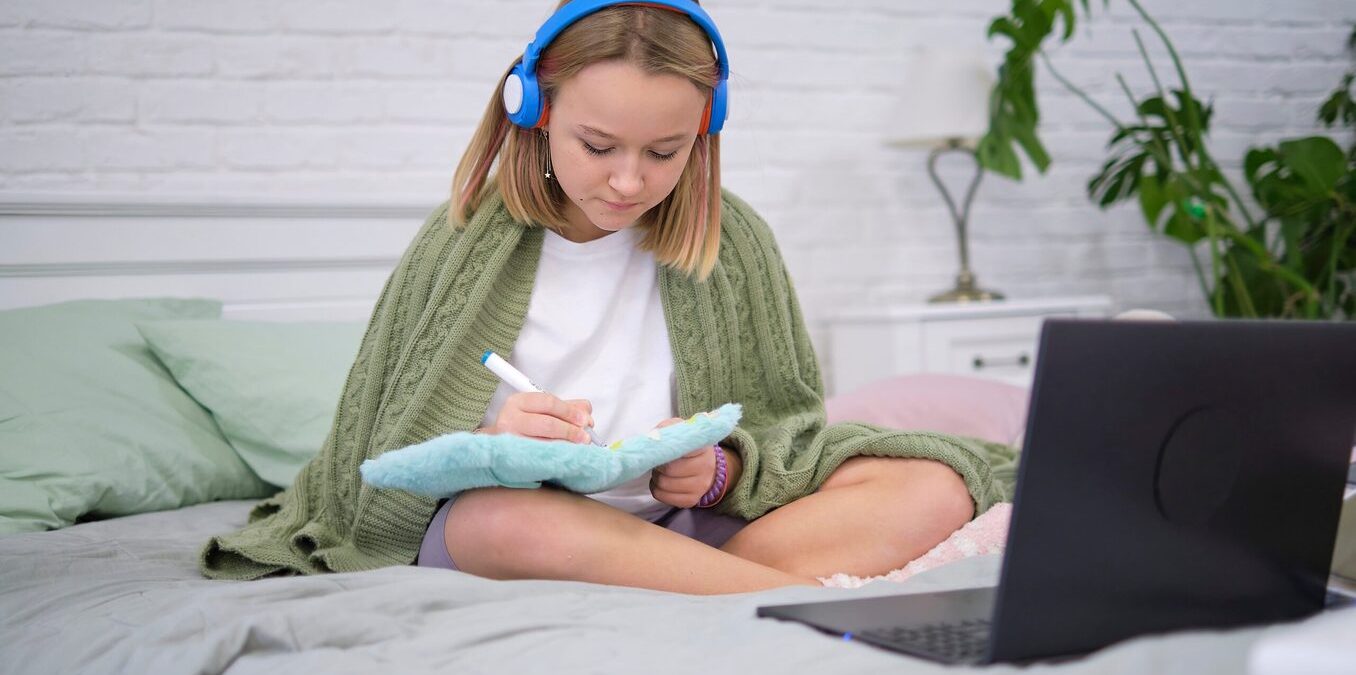 Teenage girl doing homework on the bed.