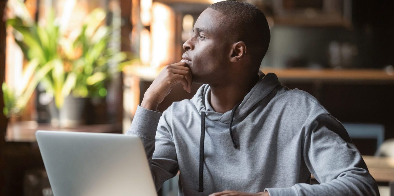 Thoughtful African American businessman lost in thoughts search for inspiration sit at cafe table using laptop