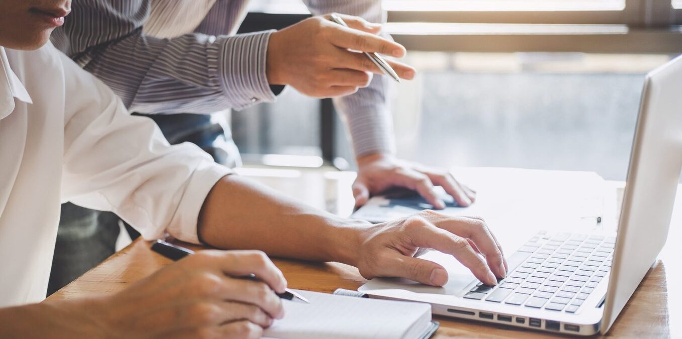 Professionals working together in front of a laptop and notebook