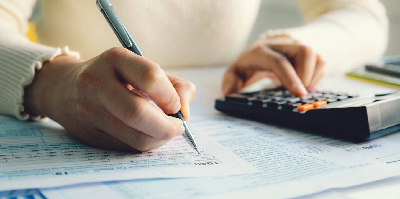 Woman filling out taxes while using a calculator on the side