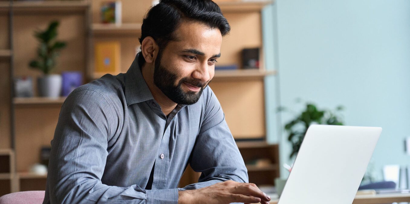 Smiling Indian business man working on laptop at home office.